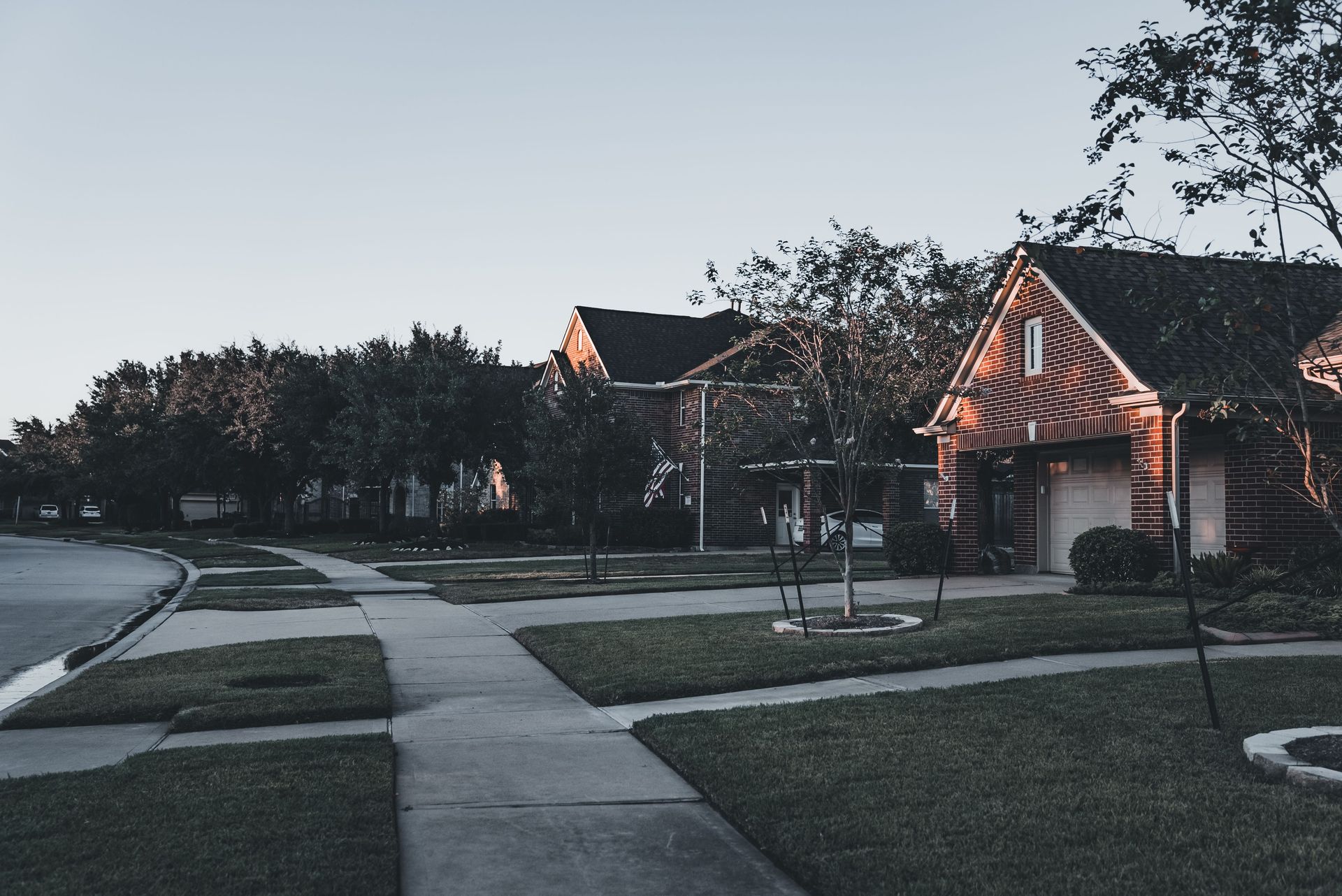 A serene suburban scene featuring brick houses and landscaped lawns at dusk.